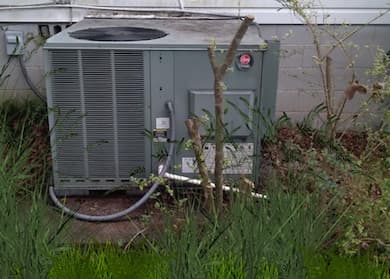 Central Air Conditioning System Surrounded by Grass and Tree limbs